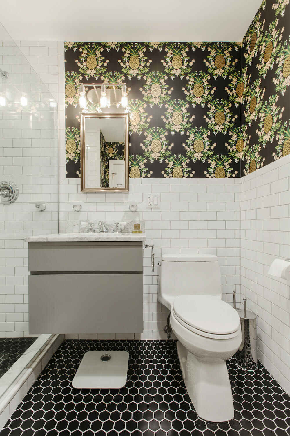 Le coin d'une salle de bain avec carrelage hexagonal noir et papier peint ananas doré.