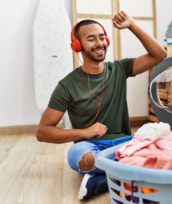 iStock-1351843702 productivité hacks jeune homme écoutant de la musique et faisant la lessive