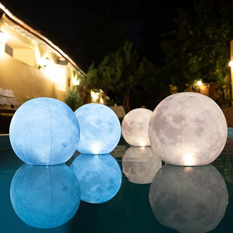 Des lampes en forme de lune et à motifs flottent dans une piscine la nuit. 