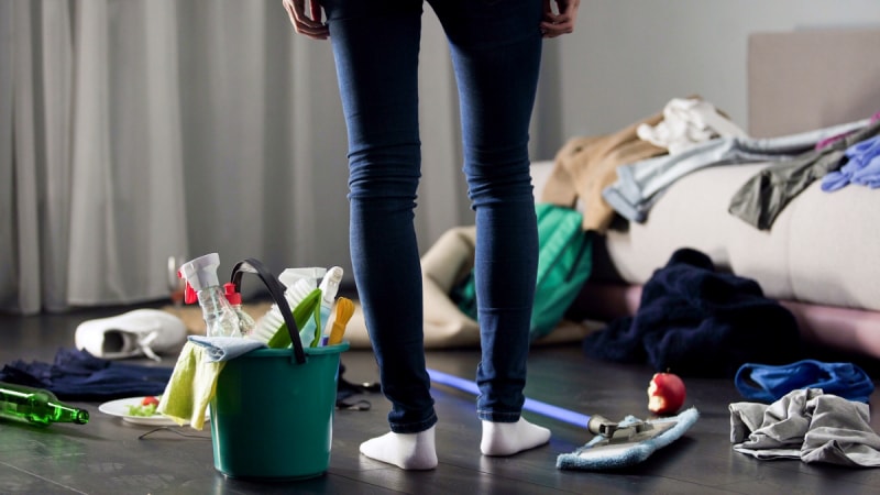 Femme debout dans une maison encombrée avec des produits de nettoyage