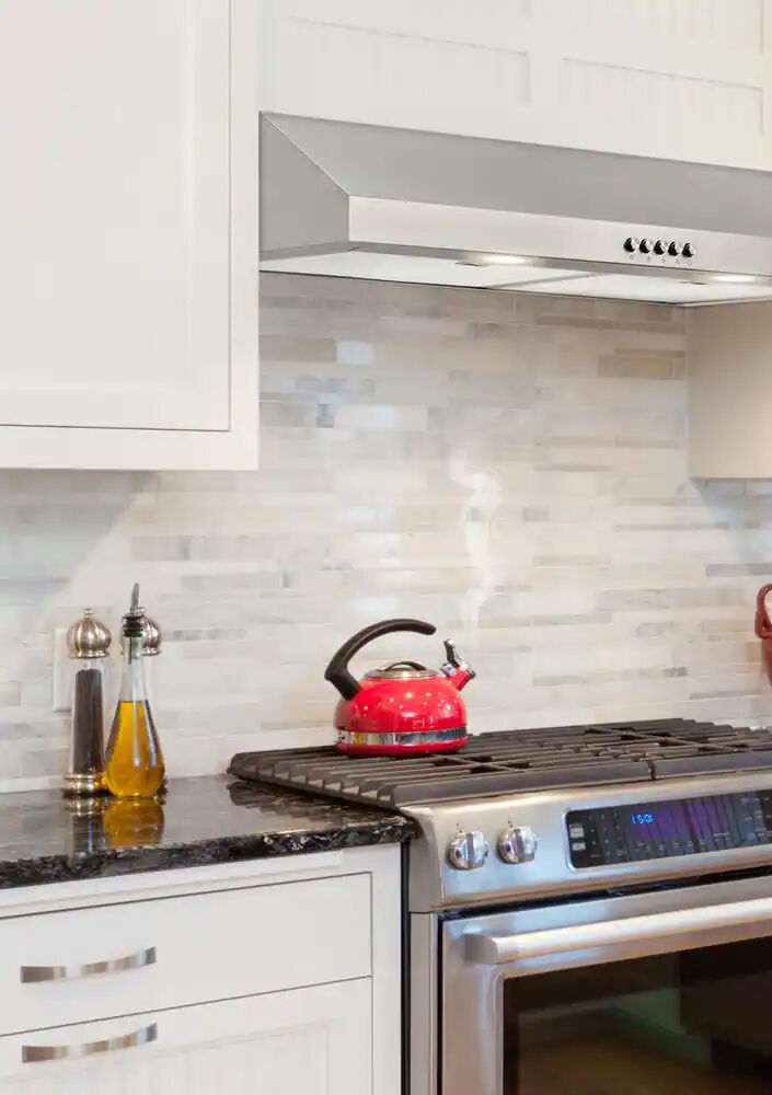 Une hotte de cuisinière en acier inoxydable sous une armoire dans une cuisine blanche.