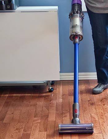 Une personne passe l'aspirateur sur un sol en bois dur avec l'aspirateur-balai Dyson V15 Detect