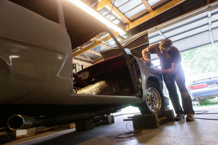 Un homme âgé travaille sur une voiture dans le garage de la maison avec la porte ouverte.