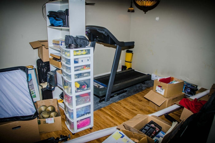 Une pièce en désordre dans un sous-sol fini qui contient du matériel de gymnastique, des boîtes en carton et des organisateurs en plastique remplis d'effets personnels.