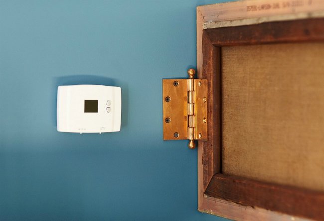 Thermostat à charnière dissimulant le tableau