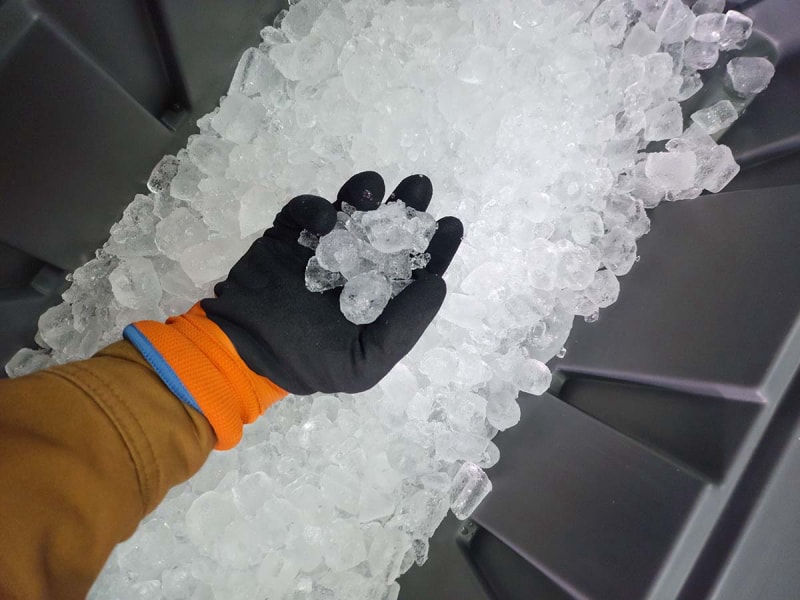 Une personne prenant une poignée de glaçons dans une machine à glaçons commerciale tout en portant les meilleurs gants de travail d'hiver.