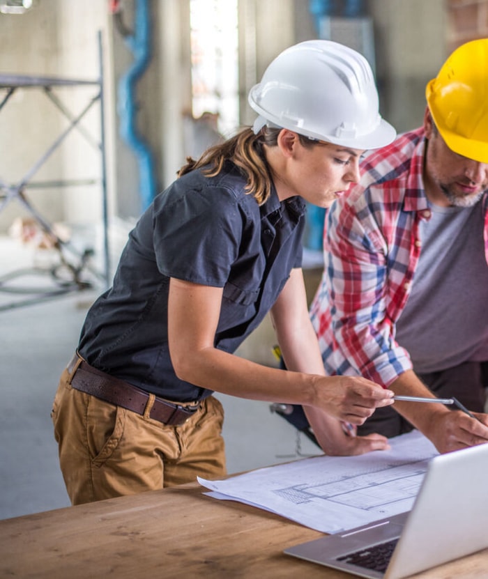 Une architecte et une contremaîtresse de chantier examinent un plan tout en utilisant un ordinateur portable sur un chantier de construction.