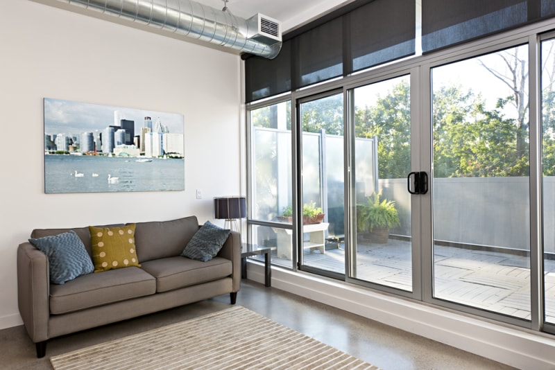 Portes coulissantes en verre installées dans un salon avec un canapé à l'intérieur et une vue sur un petit espace extérieur.