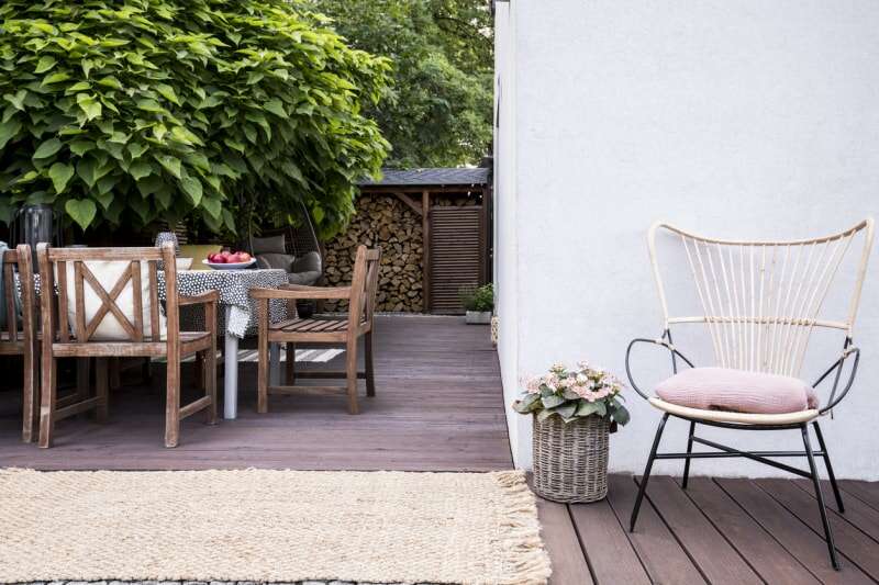 Fleurs roses près d'un fauteuil sur une terrasse en bois avec des chaises à table près d'un arbre