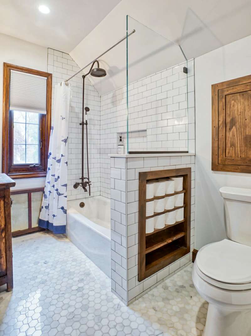 Une salle de bain blanche avec des étagères en bois intégrées remplies de rouleaux de papier toilette.