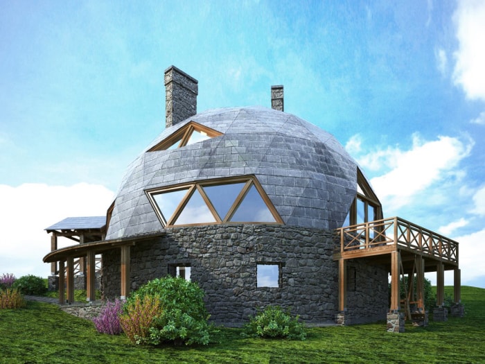 Une maison en forme de dôme avec des fenêtres triangulaires et une terrasse en bois enveloppante se dresse sur une colline verdoyante.