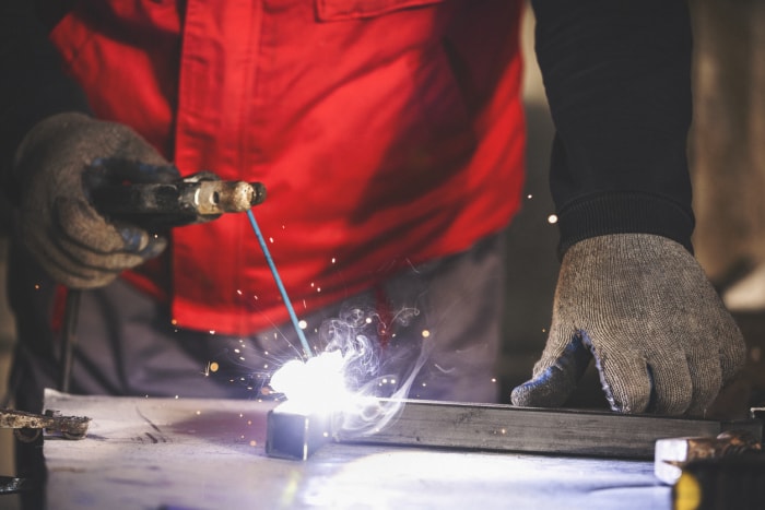 Soudeur portant des gants soudant une barre d'acier au MIG