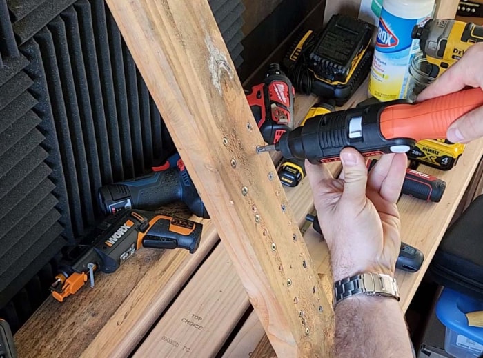 Une personne teste la meilleure option de tournevis sur un morceau de bois avec plusieurs autres tournevis électriques sur une table à l'arrière-plan.