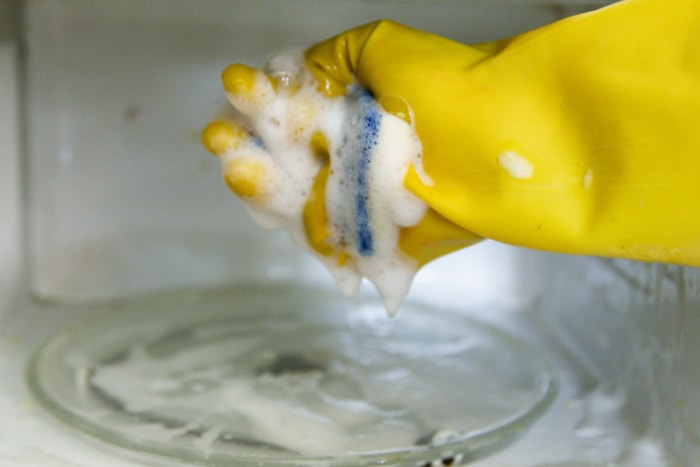 comment nettoyer un micro-ondes en utilisant des gants jaunes et une éponge pour laver le micro-ondes avec de la mousse de savon à vaisselle