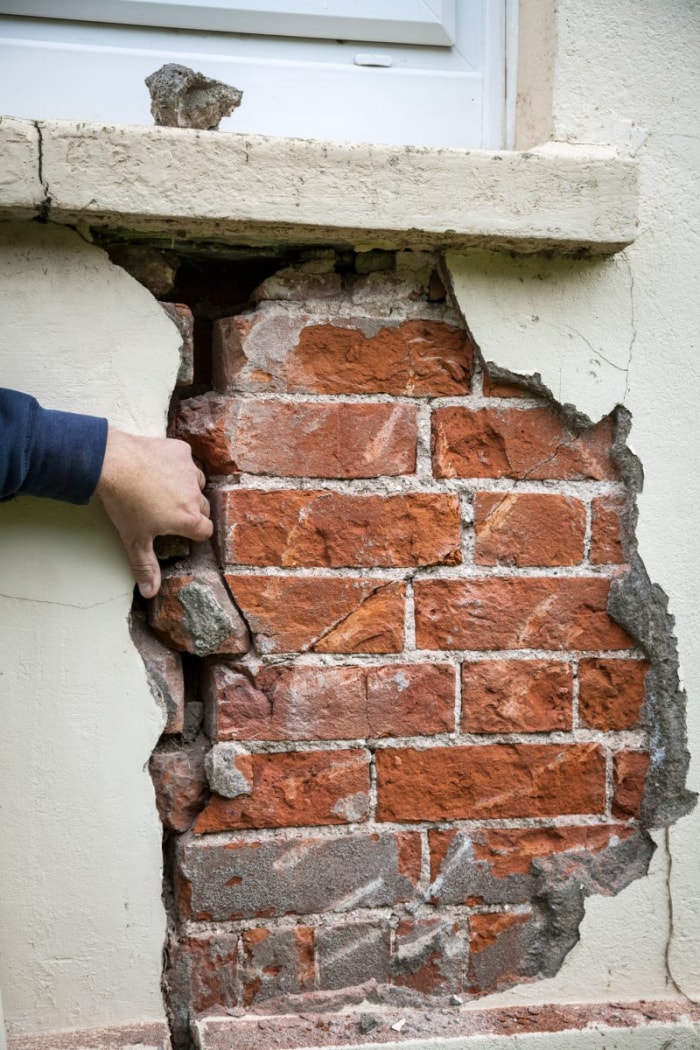 Un géomètre examine une grande fissure dans le mur d'un bâtiment en briques.