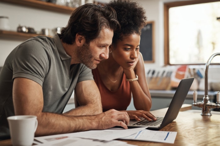 crédits d'impôt pour l'amélioration de l'efficacité énergétique de l'habitat - homme et femme regardant un ordinateur portable dans la cuisine avec des papiers sur le comptoir