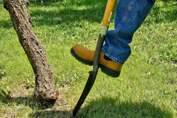 Personne portant des bottes de travail Ariat turbo chelsea marchant sur la lame d'une pelle dans l'herbe