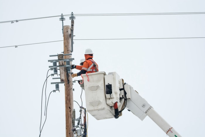 Deux ouvriers réparent des lignes électriques. 