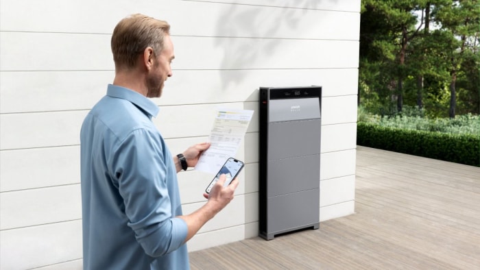 Un homme lit une facture de services publics à l'extérieur d'une maison à côté du système de stockage d'énergie Solix X1 d'Anker