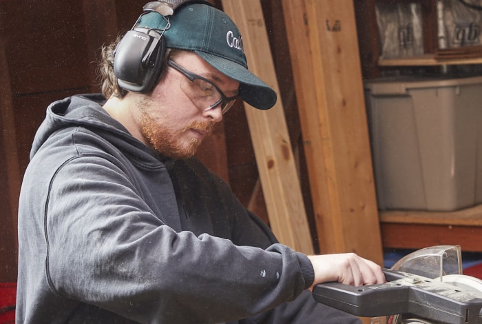 Homme utilisant une scie à onglet portant des lunettes de sécurité et une protection auditive.