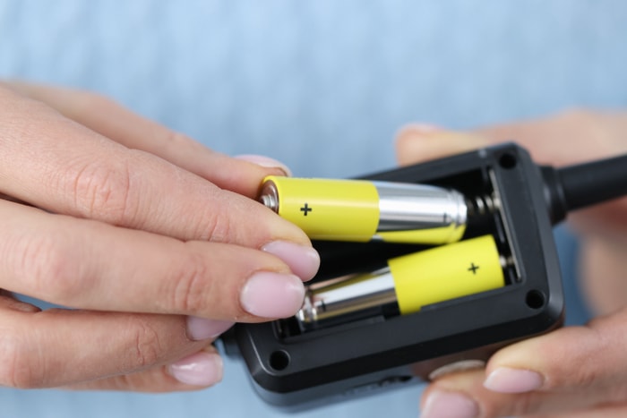 Une femme avec du vernis à ongles rose change les piles de la télécommande.