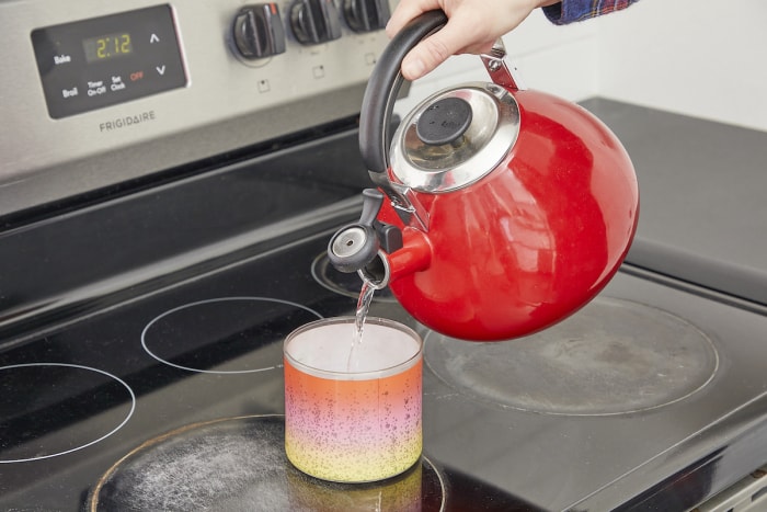 Femme versant l'eau bouillante d'une bouilloire rouge dans un photophore.