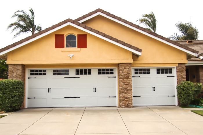 Portes de garage blanches et propres sur une maison jaune.