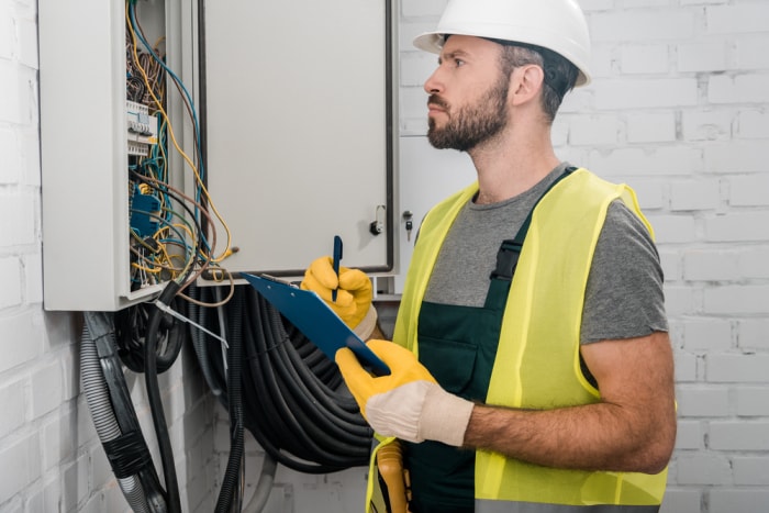 Un ouvrier a l’air pensif alors qu’il évalue un panneau électrique. 