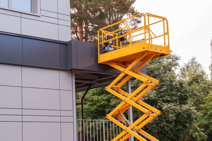 Vue d'un élévateur à ciseaux à côté d'un bâtiment gris. 