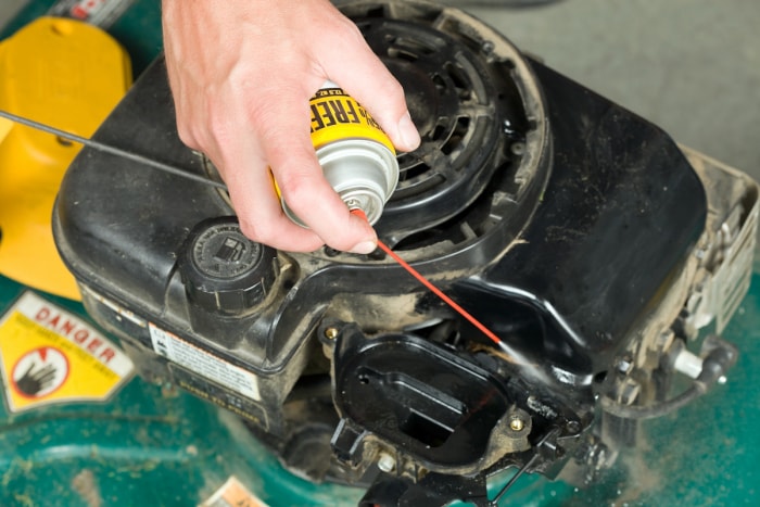 Une personne utilise une bombe d’air comprimé pour nettoyer le carburateur d’une tondeuse à gazon.