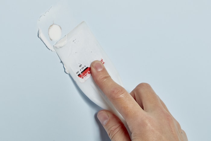 Une femme utilise un couteau à mastic en plastique pour gratter l'excès de mastic d'un mur.