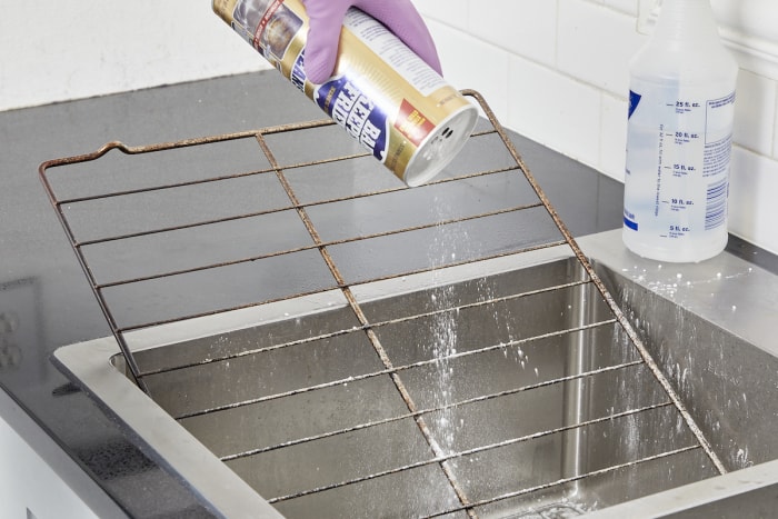 Une femme verse du Bar Keepers Friend sur la grille du four dans un évier en acier inoxydable.