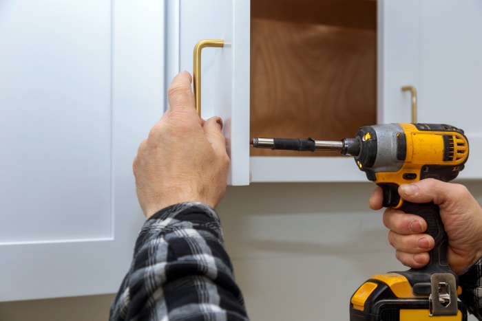 Une personne utilise un outil électrique pour installer une nouvelle poignée d'armoire