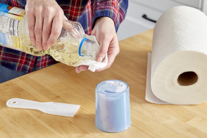 Une femme utilise de l’huile de cuisson sur une serviette en papier pour retirer un autocollant d’une tasse.