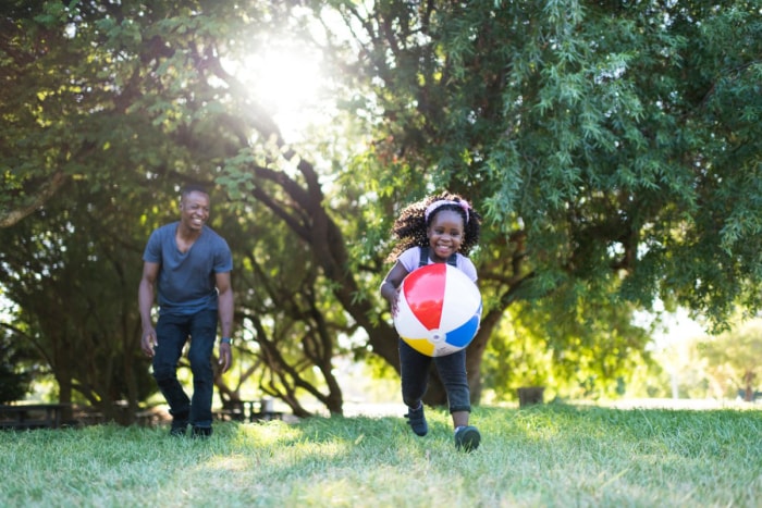 Petite fille heureuse jouant avec un ballon de plage dans l'herbe avec son père