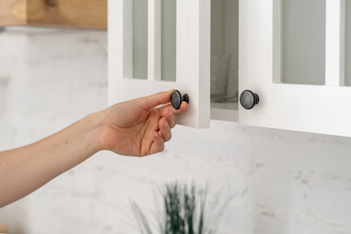 Vue recadrée de la main d'une femme ouvrant la porte d'un meuble blanc, dans une maison à l'intérieur moderne.