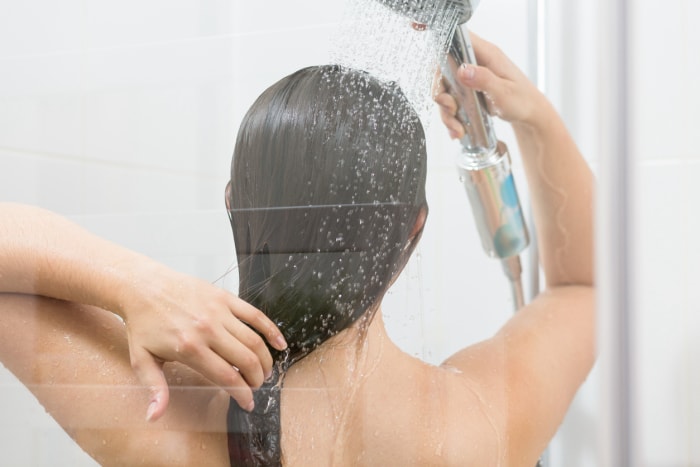 l'arrière de la tête d'une femme alors qu'elle se lave les cheveux avec un robinet de douche à main