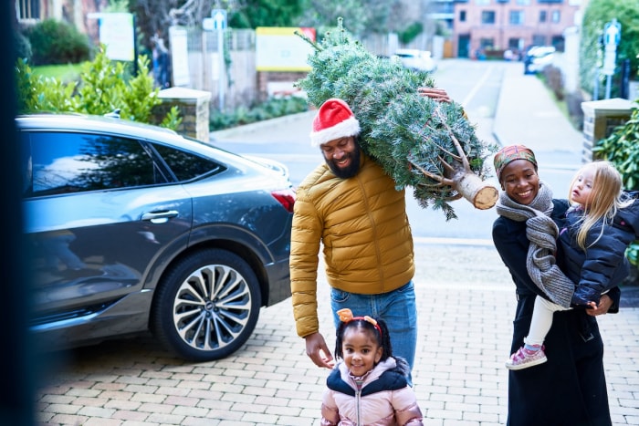 Une famille entrant dans sa maison avec un sapin de Noël fraîchement coupé.