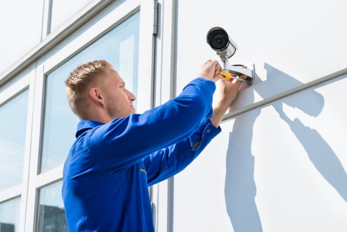 Gros plan d'un ouvrier installant une caméra de sécurité à l'extérieur d'une maison. 