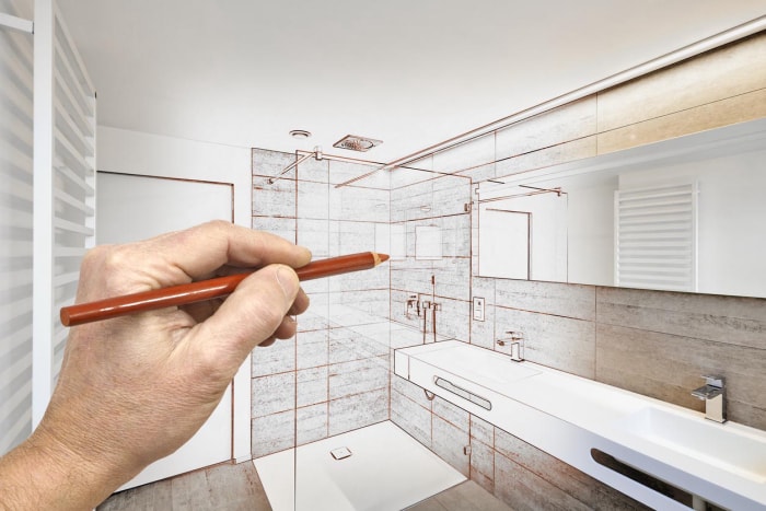 Gros plan d'une main tenant un crayon rouge et l'utilisant pour concevoir une nouvelle douche. 