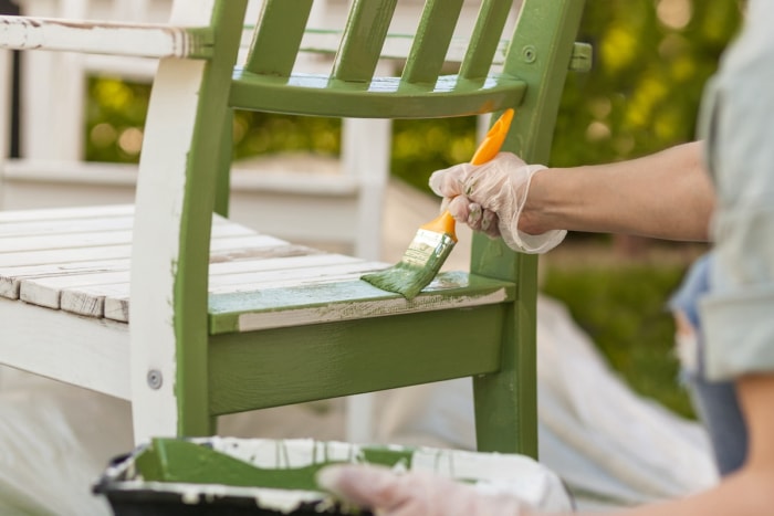 Une personne peignant une chaise de patio en bois avec de la peinture verte pour meubles d'extérieur.