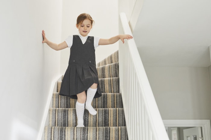 Une jeune fille descend un escalier recouvert de moquette avec un motif à rayures de couleur neutre.