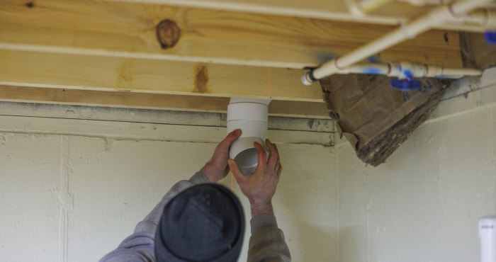 Installation d'un système d'atténuation du radon. Un ouvrier installe un tuyau dans le plafond du sous-sol.