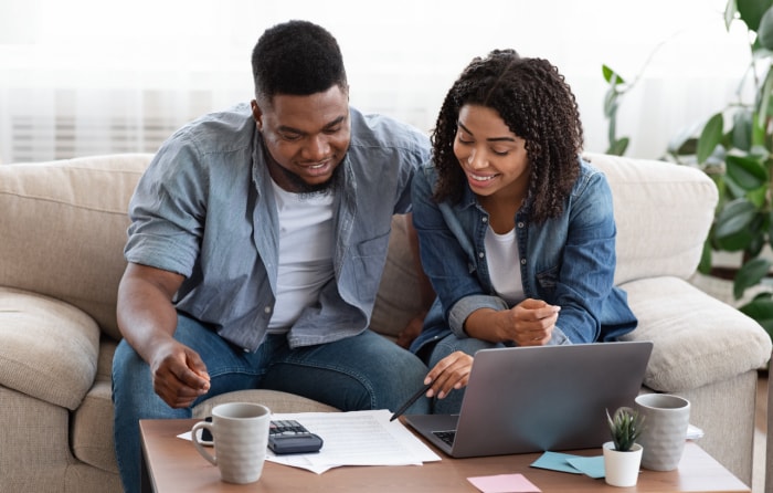 un jeune couple est assis sur le canapé devant la fenêtre, avec un ordinateur portable et des documents financiers sur la table basse, travaillant ensemble