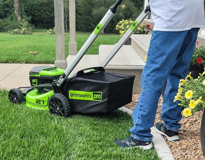 Une personne utilisant la tondeuse à batterie Greenworks Pro 60V 21 pouces pour tondre une pelouse d'un vert éclatant.