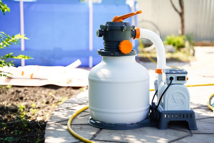 Système de filtration à sable blanc et orange à côté d'une piscine hors-sol