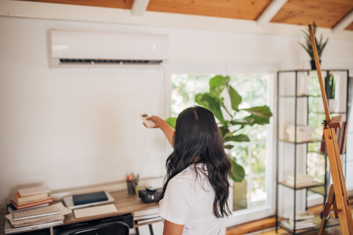 femme au bureau à domicile utilisant une télécommande pour allumer le climatiseur fixé au mur