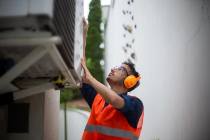 Un travailleur portant un gilet de sécurité orange inspecte un climatiseur.