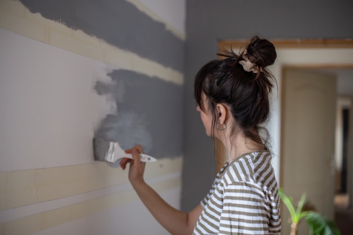 Femme peignant un mur gris avec des traces de pinceau