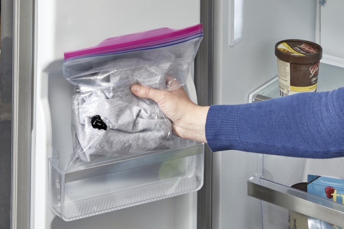 Une femme met des vêtements dans un sac Ziploc dans le congélateur.